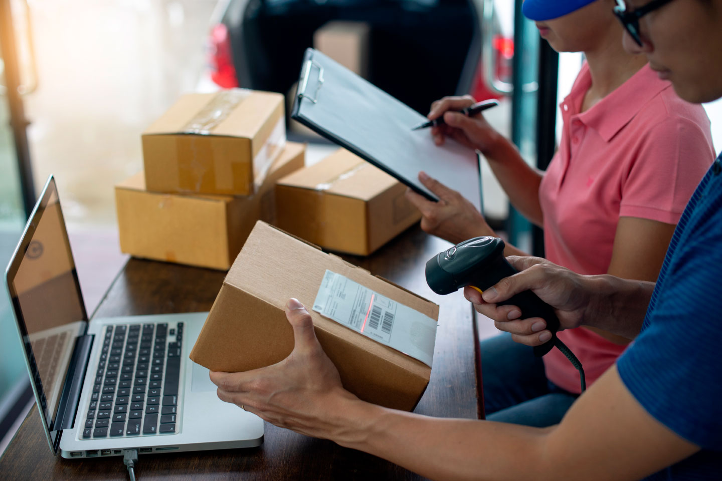 Warehouse workers checking packages with a clipboard, barcode scanner and laptop